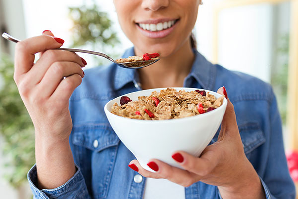 Close-up of smiling young woman eating breakfast cereals of bowl at home.